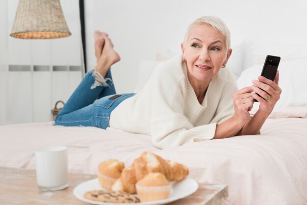 Donna matura di smiley a letto che tiene smartphone