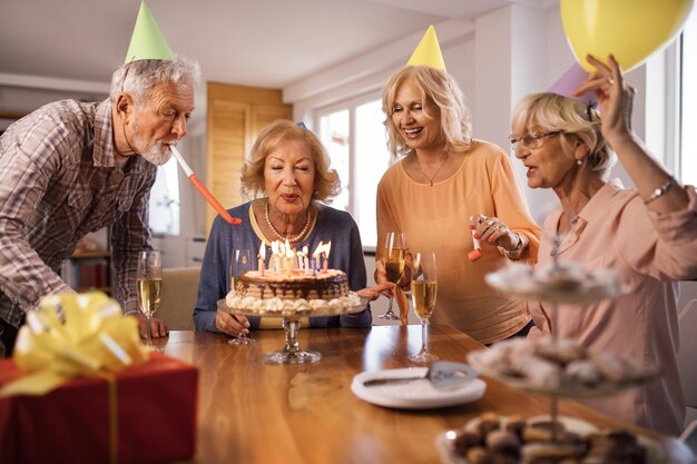 Donna matura felice che celebra il compleanno con i suoi amici e soffia le candeline su una torta a casa