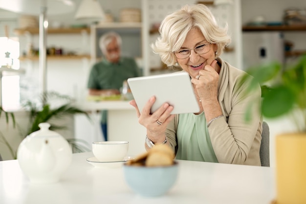 Donna matura felice che utilizza tablet digitale a casa
