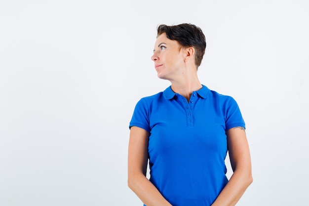 Donna matura in maglietta blu che osserva da parte e che sembra concentrata, vista frontale.