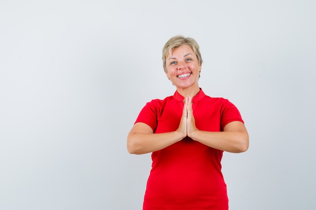 Donna matura in maglietta rossa che mostra il gesto di namaste e che sembra felice