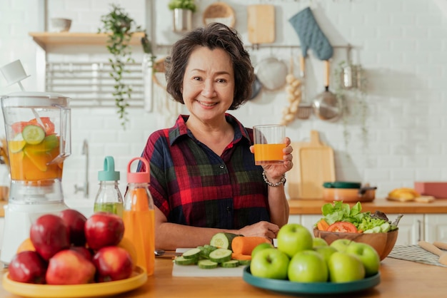 Donna matura sorridente cucinare insalata di frutta e verdura Donna matura attraente con insalata di frutta fresca verde a casa Grembiule da donna senior in piedi nel bancone della cucina rilassante in casa tempo di fine settimana