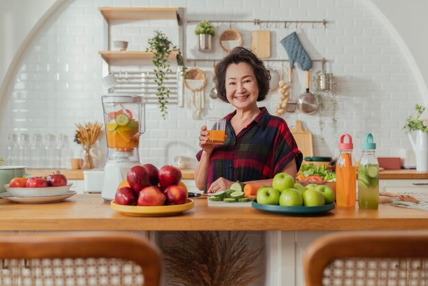 Donna matura sorridente cucinare insalata di frutta e verdura Donna matura attraente con insalata di frutta fresca verde a casa Grembiule da donna senior in piedi nel bancone della cucina rilassante in casa tempo di fine settimana