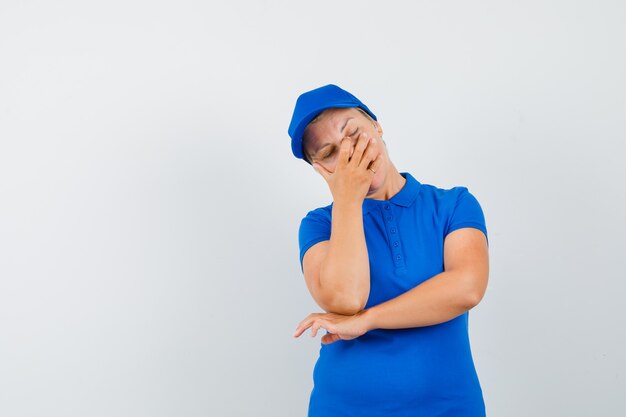 Donna matura tenendo la mano sul viso in maglietta blu e guardando deluso.