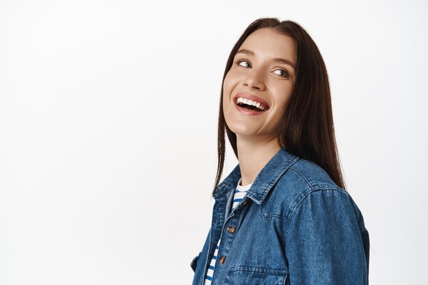 donna, modella bruna che ride e sorride denti bianchi, pelle pulita e luminosa di una femmina adulta, guardando da parte spensierata, in piedi sul bianco