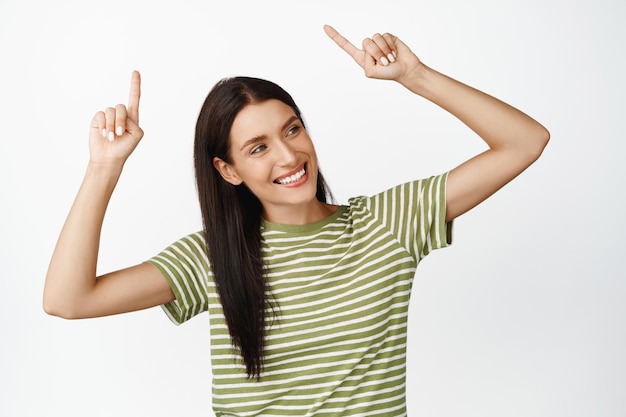 Donna moderna eccitata che punta le dita verso l'alto sorridendo come mostra lo sfondo bianco dell'insegna del negozio di pubblicità