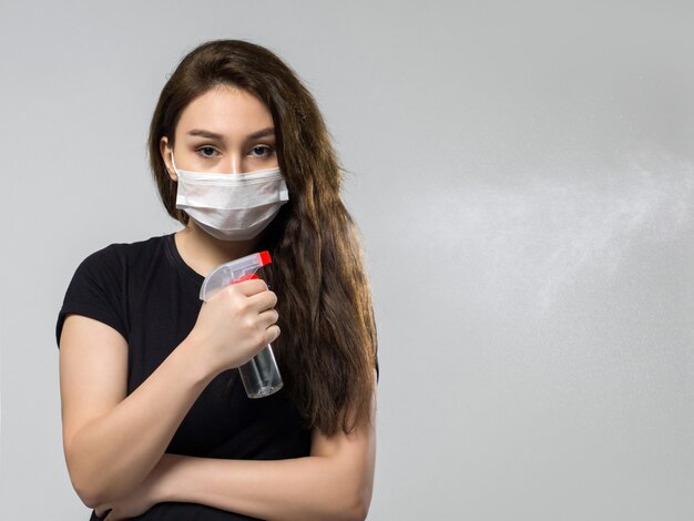 Donna nella mascherina medica sterile protettiva bianca che tiene spruzzo disinfettante speciale