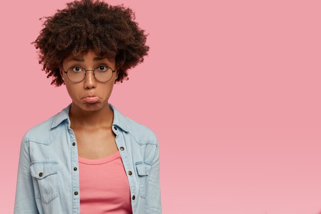 donna offensiva delusa porta il labbro inferiore, discute con il marito, si sente triste e frustrata, ha la pelle scura, i capelli ricci, modelle su un muro rosa con spazio libero per il testo