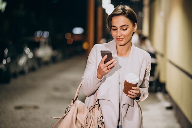 Donna parla al telefono e bere caffè fuori in strada di notte