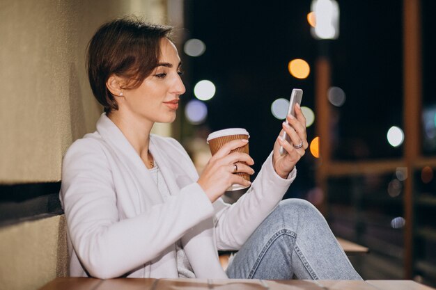 Donna parla al telefono e bere caffè fuori in strada di notte