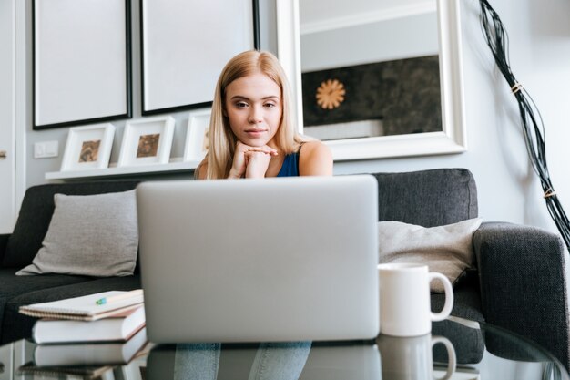 Donna pensierosa che pensa e che per mezzo del computer portatile a casa