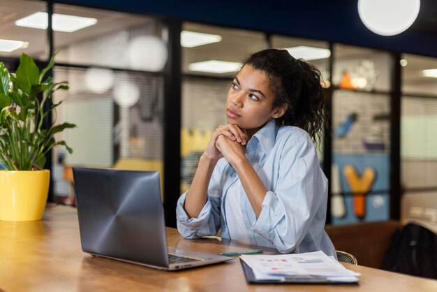 Donna pensierosa in ufficio con il computer portatile