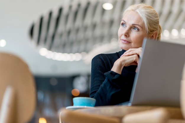 Donna più anziana di affari che mangia caffè e lavora al computer portatile