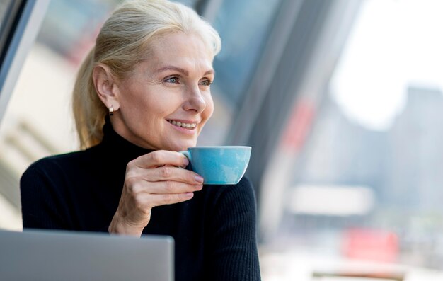 Donna più anziana di affari di smiley che mangia caffè all'aperto mentre lavora