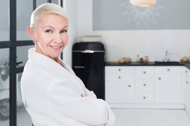 Donna più anziana di smiley che posa in accappatoio nella cucina