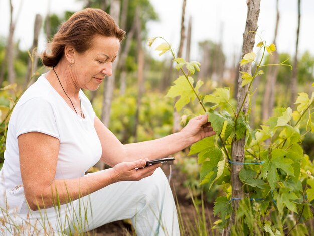 Donna più anziana di vista laterale che resta accanto ad una pianta nel suo giardino