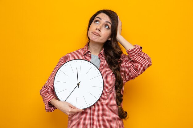 Donna più pulita caucasica confusa che tiene l'orologio e si mette la mano sulla testa guardando in alto