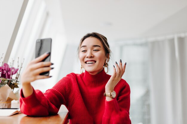 Donna positiva in maglione luminoso ride e parla in video nel telefono