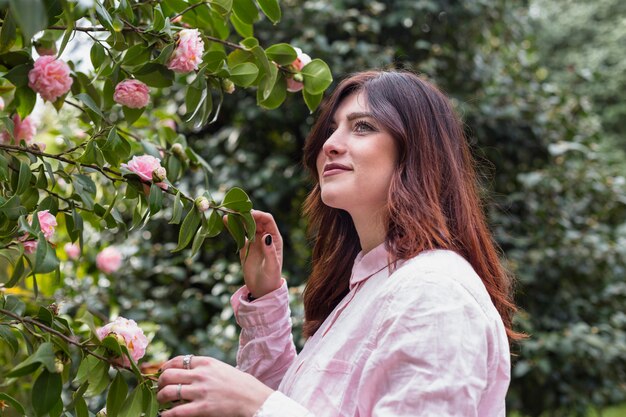 Donna positiva vicino ai fiori rosa che crescono sui ramoscelli verdi