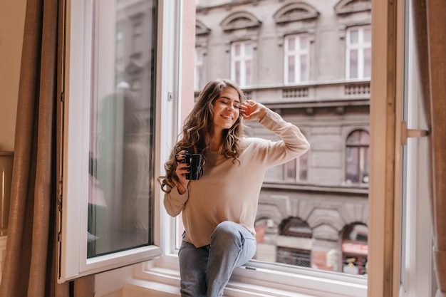 Donna raffinata in camicia alla moda che gode della vista della città dalla finestra