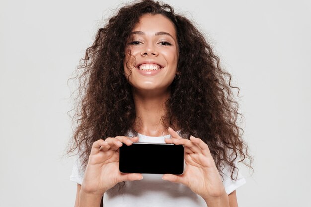 Donna riccia sorridente che mostra lo schermo in bianco dello smartphone