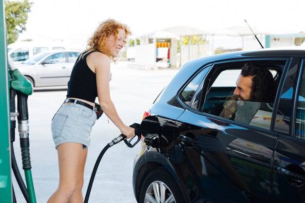 Donna riempiendo auto e sorridente per amico alla stazione di gas