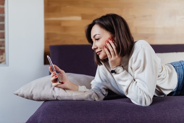 Donna rilassata che per mezzo di uno Smart Phone che si trova su un letto a casa