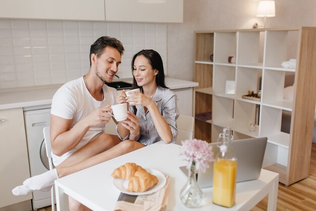 Donna romantica in calzini bianchi agghiacciante con il marito durante la colazione e godersi i croissant