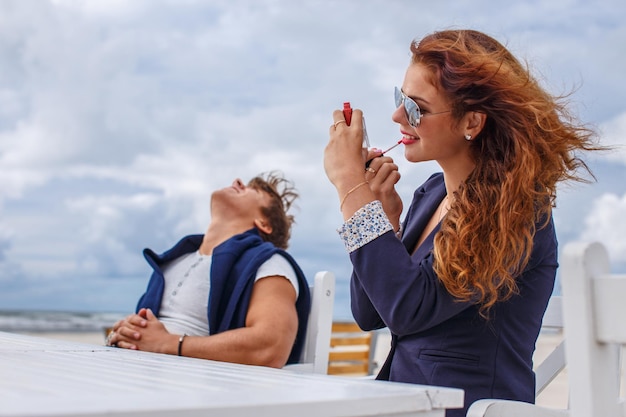 Donna rossa e un ragazzo seduto al tavolo sulla spiaggia.