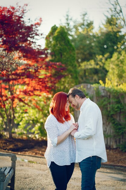 donna rossa in una camicetta bianca in piedi in un parco di sole estivo con il suo fidanzato