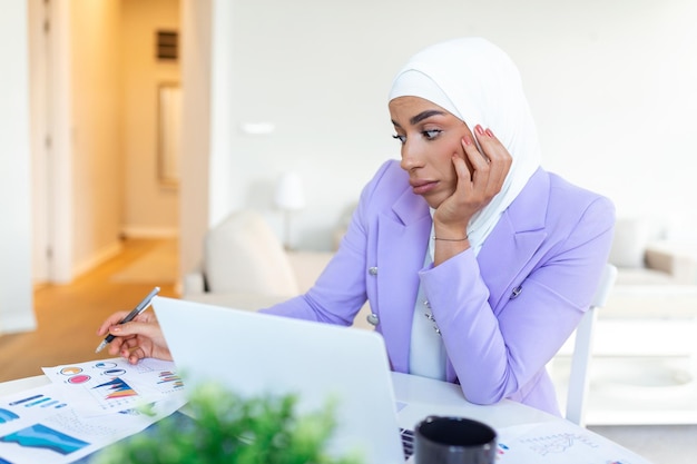 Donna sconvolta che indossa l'hijab davanti al laptop cerca e fa lavoro d'ufficio finanza aziendale e concetto di workstation Donna d'affari araba che lavora a casa