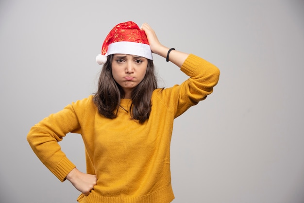 Donna sconvolta in cappello rosso di Babbo Natale in posa su un muro bianco.