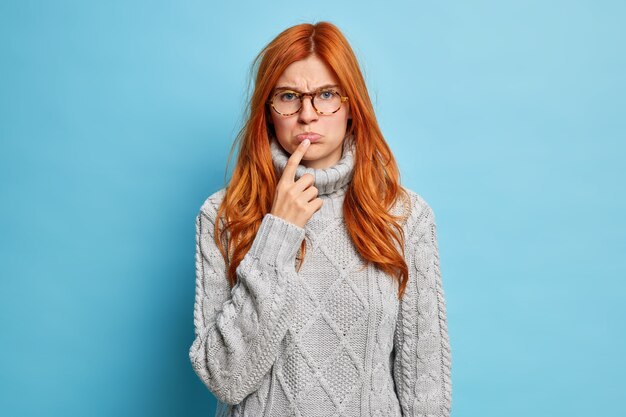 donna sconvolta offesa tiene il dito indice sulle labbra sembra infelicemente vestita in maglione lavorato a maglia grigio.