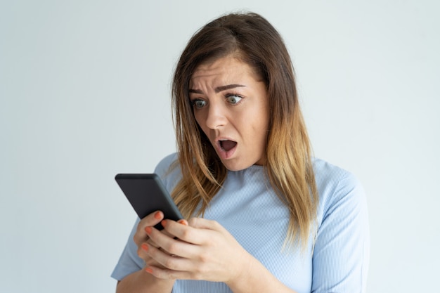 Donna scossa che tiene smartphone e guardando il suo schermo. Messaggio di lettura della signora