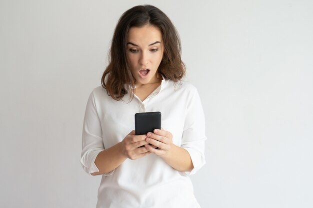 Donna scossa che tiene smartphone e guardando il suo schermo