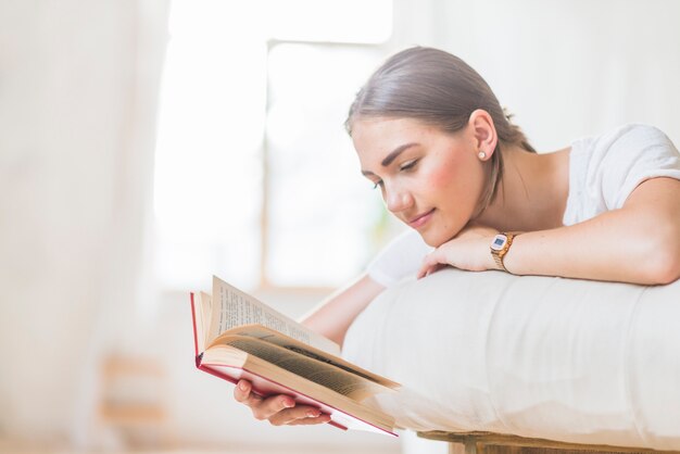 Donna sdraiata sul letto a leggere il libro a casa