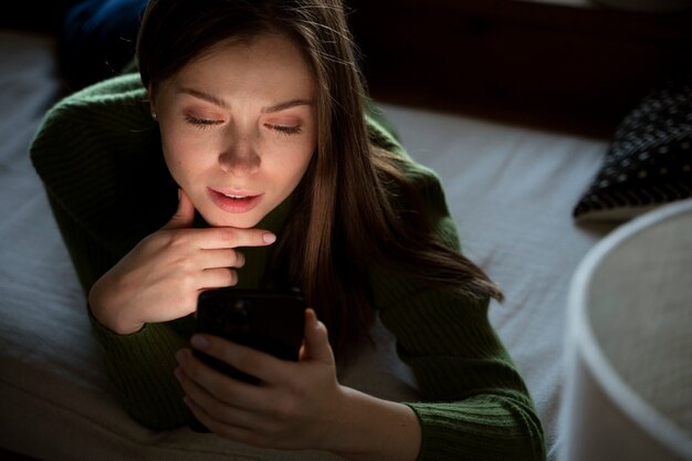 Donna sdraiata sul letto mentre guarda il suo smartphone