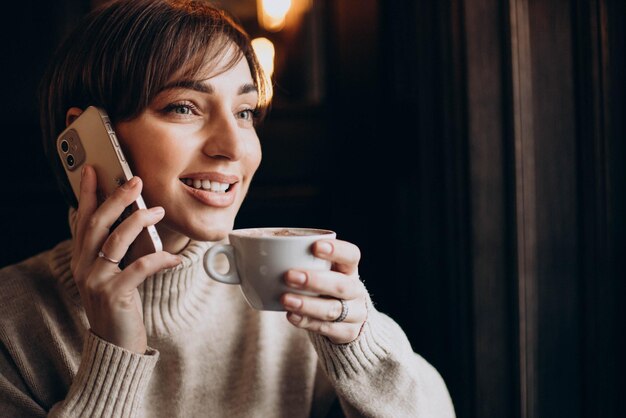 Donna seduta in un bar e bere caffè e parlare al telefono