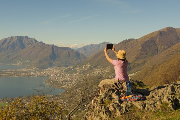 Donna seduta su una montagna e scattare foto della splendida vista sul lago in Svizzera