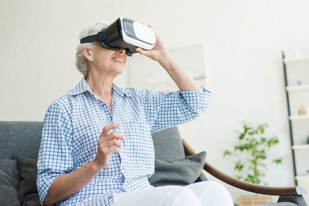 Donna senior che si siede sul sofà che gode dei vetri di realtà virtuale