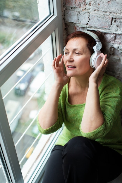 Donna senior dell'angolo alto accanto a musica d'ascolto della finestra