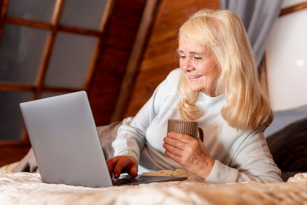 Donna senior di angolo basso a letto facendo uso del computer portatile