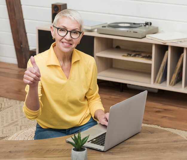 Donna senior di smiley dell'angolo alto che per mezzo di un computer portatile