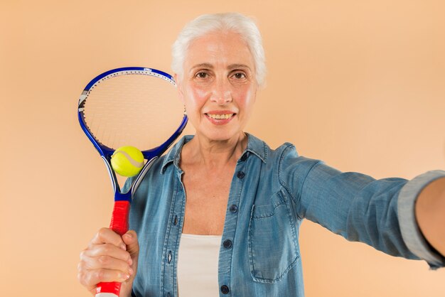 Donna senior moderna con la racchetta di tennis che prende selfie