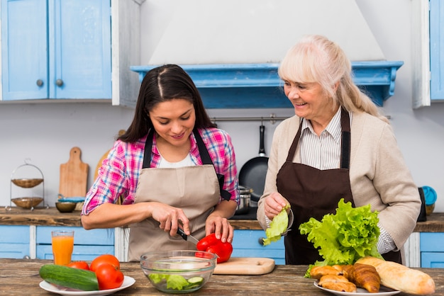 Donna senior sorridente che esamina la verdura di taglio della figlia nella cucina