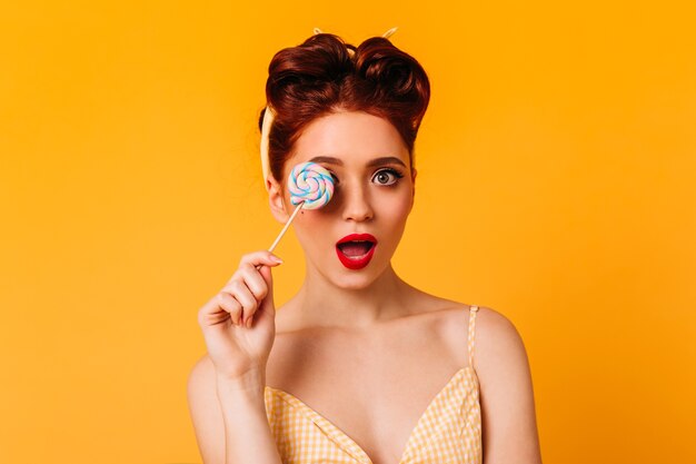 Donna sensuale sorpresa che tiene lecca-lecca. Studio shot di attraente ragazza pinup con caramelle dolci.