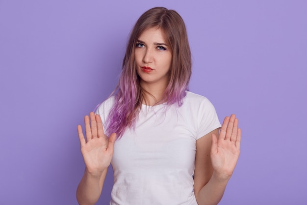 Donna seria che mostra i palmi alla telecamera, guardando con severo gesto di espressione e divieto, proibisce a qualcuno di fare cose cattive, isolato sopra il muro viola.