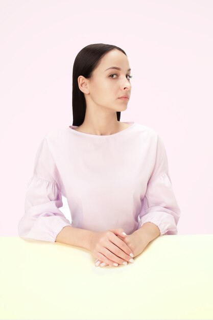 Donna seria di affari che si siede al tavolo su uno sfondo rosa studio. Il ritratto in stile minimalista