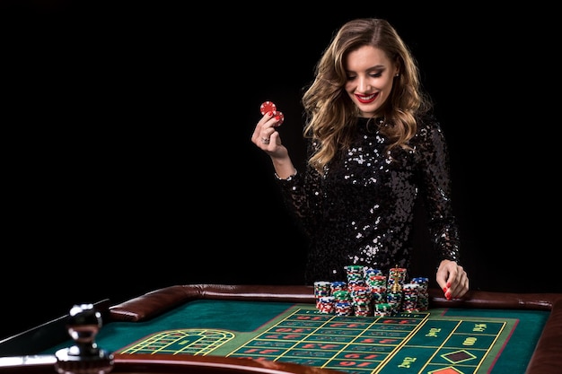 Donna sexy in un vestito nero che gioca nel casinò. La donna punta pile di fiches giocando alla roulette al club del casinò. Gioco d'azzardo. Roulette.