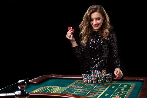 Donna sexy in un vestito nero che gioca nel casinò. La donna punta pile di fiches giocando alla roulette al club del casinò. Gioco d'azzardo. Roulette.